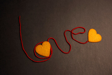 Love word written by red thread with two hearts on black background 