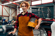 © DusanJelicic - Woman with curly red hair standing in workshop, holding protective equipment under arm and smiling at camera, workshop in background