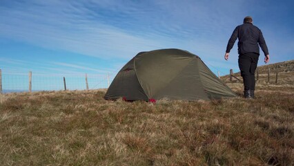 Wall Mural - A man closing a wild camping tent and walking away into the hills