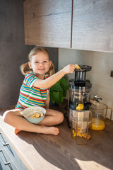 Wall Mural - Little girl making fresh juice sitting on the table in home kitchen