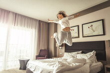 Woman Having Fun And Jumping With Bathrobe On Bed In Hotel Room