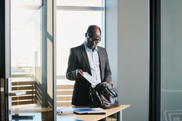 Aufkleber - Serious mature director of business company putting documents into leather handbag while standing by desk in office or boardroom
