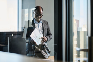 Poster - Serious mature African American chief executive office putting papers into bag while leaving for meeting with important businesspeople