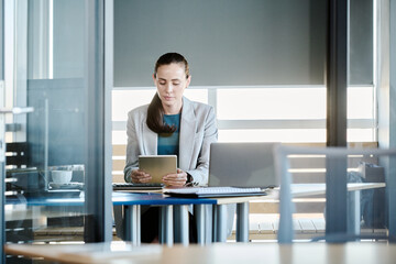Poster - Young serious businesswoman or intern with tablet sitting in office and watching video about starting and developing new business