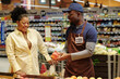 © pressmaster - Happy young African American male sales assistant advising female customer new sort of apples in grocery department