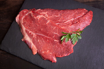 Raw minute steak of marbled beef with a parsley leaf on a stone slate board