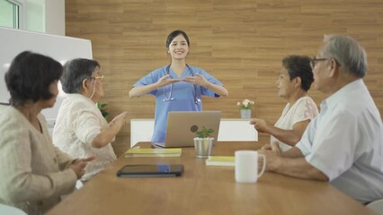 Wall Mural - An Asian nurse talking to a group of old elderly patient or pensioner people smiling, relaxing, having fun together in nursing home. Senior lifestyle activity recreation. Retirement. Health care