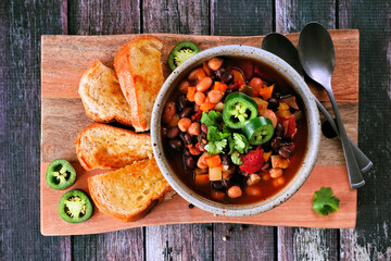 Wall Mural - Homemade vegetarian chili with garlic bread on a wooden serving board. Top view table scene on a dark wood background.
