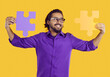 Joyful Indian man connects two colored pieces of puzzles that symbolize solution to problem. Happy man in purple shirt and glasses on orange background holds two pieces of puzzle that match each other