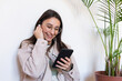 © ADDICTIVE STOCK - Cheerful woman in earphones browsing smartphone at home
