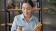 © RZ Images - Close up portrait of smiling asian business woman pays for online purchases by card using the smartphone
