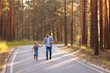 © Kaplitskaya Love - Dad and his little daughter are walking along a forest road among tall pines. Family walk in the forest at sunset, man and little girl.