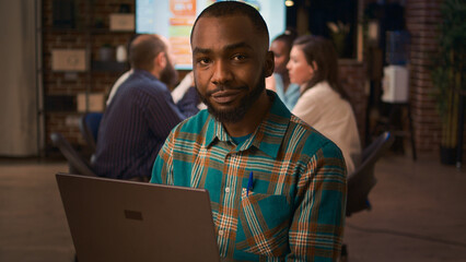 Poster - african american smiling employee working on laptop portrait, slow motion, front view. office worker