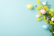 Easter Concept. Top View Photo Of Colorful Easter Eggs Yellow Mimosa Flowers And Butterflies On Isolated Pastel Blue Background With Copyspace