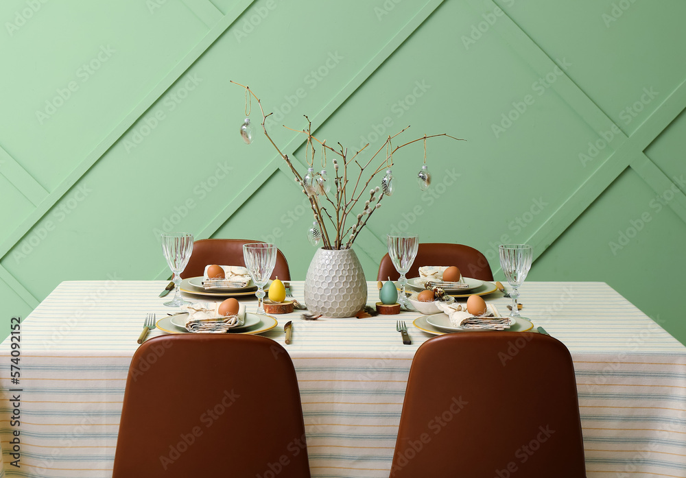 Festive dining table with eggs and pussy willow branches served for Easter celebration near green wall