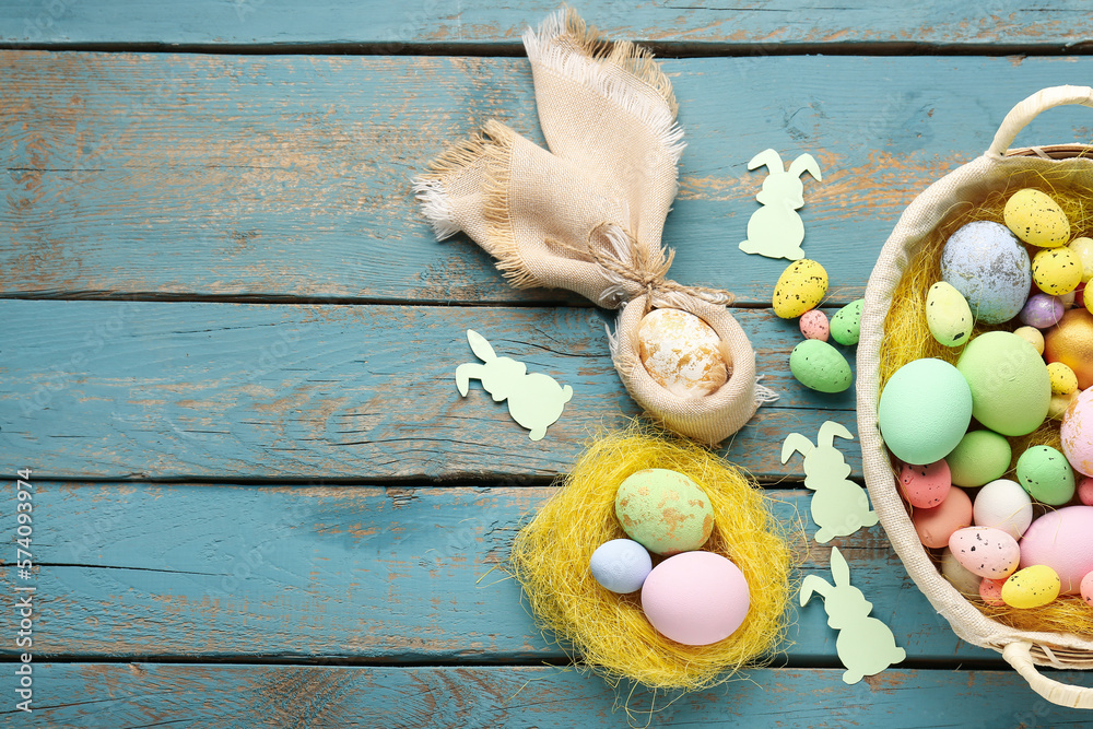 Basket with Easter eggs and paper rabbits on blue wooden background