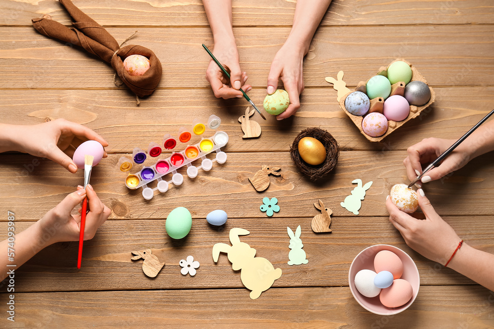 Women painting Easter eggs on wooden background, top view