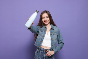 Poster - Beautiful young woman with thermos bottle on purple background