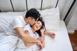 Asian husband kissing his wife while lying down sleep on bed in bedroom