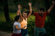 © La Famiglia - Group of runners running marathon outdoors. They are running in the mountains at sunset. Wearing sports clothes. Smiling. Running through the finish with arms raised.
