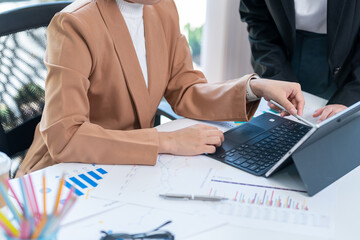 Wall Mural - Two young Asian business women meet to analyze the financial chart at the office to discuss the financial situation at the company. A partner sits at a desk with modern documents and equipment.