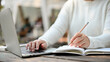 © bongkarn - Female working on a project remotely at the cafe, using a laptop, and noting something in a book.
