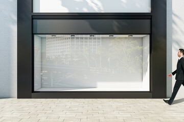 Poster - Businessman walking through sunlit empty showcase with light wall background behind window with space for product presentation in modern business center building outdoors, mock up