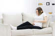 © Andrii - Pregnant woman put her hands on her stomach on white sofa.