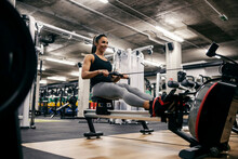 A strong healthy sportswoman is doing workouts on a rower machine in a gym.