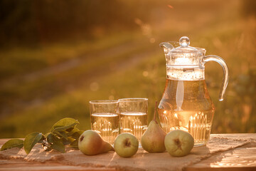 Two glasses with pear juice and basket with pears on wooden table with natural orchard background on sunset light. Vegetarian fruit composition