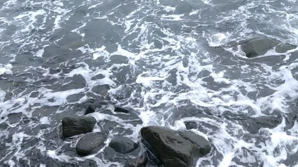 Wall Mural - The waves wash over the dark volcanic beach. Volcanic rocks.