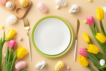 Wall Mural - Easter concept. Top view photo of empty plates cutlery colorful easter eggs ceramic bunnies yellow and pink tulips and wooden egg holder on isolated pastel beige background