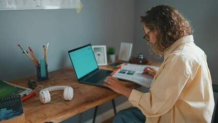 Wall Mural - Side view of curly haired serious woman studying with books and a laptop at the table at home