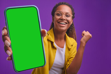 young overjoyed african american woman stretches out hand with smartphone showing off record in mobi