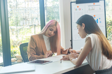 Two women analyzing documents while sitting on a table in the office