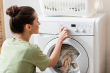 Side View Of Blurred Woman Switching Washing Machine Near Basket In Laundry Room.