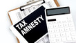TAX AMNESTY text on a tablet with chart, calculator and pen