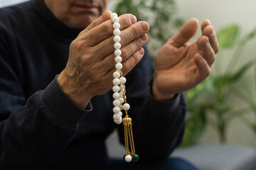 Praying hands of an old man holding rosary beads.