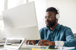 © Prostock-studio - African american male employee in glasses and wireless headphones sitting at office desk and working on computer