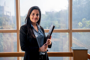 Wall Mural - Indian Corporate woman holding file in hand and giving smile expression at office.