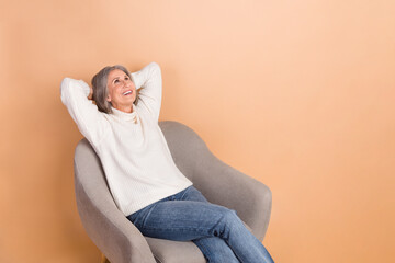 Poster - Photo of cheerful positive woman wear knitted pullover looking empty space arms behind head isolated beige color background