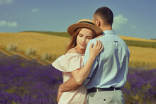 A Couple In Love In A Field Of Lavender At Sunset In Good Weather. Beautiful Woman In A Dress And Straw Panama With A Man On The Background Of Nature, Love And Feelings. Blue, Purple Lavender.