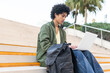 © ADDICTIVE STOCK - Focused ethnic student with backpack using laptop on stairs