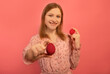 © Anastasia - Happy smiling young woman in spring floral pink dress holds two red painted easter eggs or shows dyed easter eggs isolated on pink background.Girl puts one hand forward with colored egg. Easter Day.