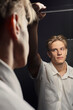 a serious man in a white shirt looks at himself in the mirror standing on a black background