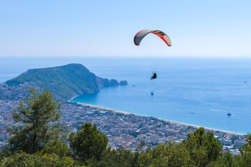 Paragliding in the sky. Paraglider tandem flying over the sea with blue water, beach and mountains in background in Alanya Turkey.