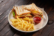 Two sandwiches with french fries and ketchup on white plate on wooden table