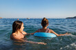 Two sisters in bathing suits play with an inflatable ring in the sea