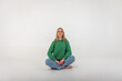 Young pretty emotional chic girl sitting on the floor in a flirtatious mood, gesturing with her hands, empty space, wearing jeans and a green sweater on an isolated white background, space for text