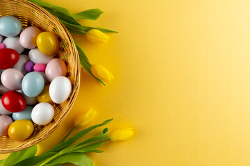Wall Mural - Image of multi coloured easter eggs in basket with yellow tulips and copy space on yellow background